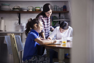 Woman looking at daughters studying seen through doorway