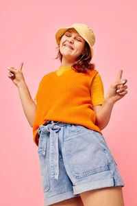 Portrait of young woman standing against pink background