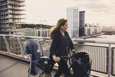 Mature woman walking with bicycle on footbridge in city