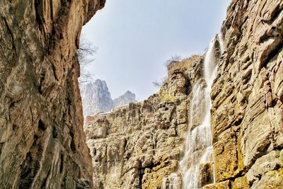 Low angle view of rocky mountains and waterfalls against sky