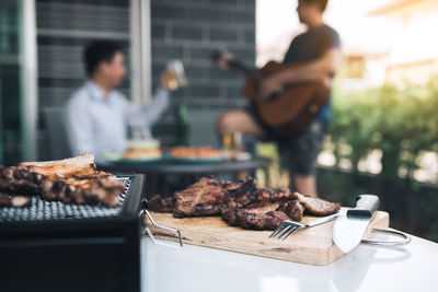 Close-up of meat on barbecue with friends in background