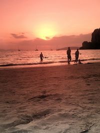 Silhouette people on beach against sky during sunset