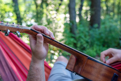 Closeup of a man's hands strumming a guitar while laying in a hammock