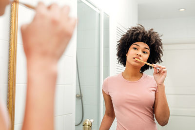 Teenage girl brushing teeth while looking in mirror at home