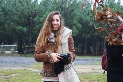 Young woman smiling while standing by tree against plants