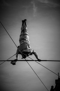 Low angle view of man sitting on rope against sky