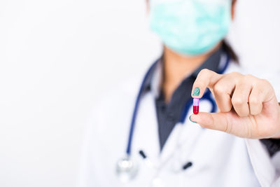 Midsection of female doctor holding pill against white background