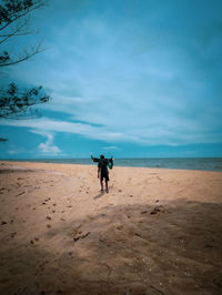 Rear view of woman walking on beach against sky