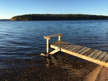 Pier on lake against clear blue sky