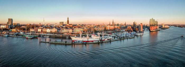 Sailboats moored in harbor by buildings against sky during sunset