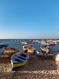 Boats moored on beach against clear blue sky