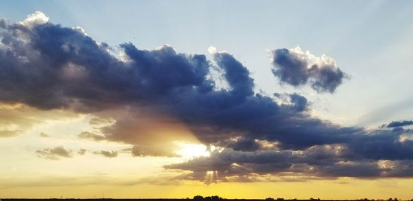 Low angle view of sunlight streaming through clouds during sunset