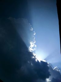 Low angle view of sunlight streaming through clouds