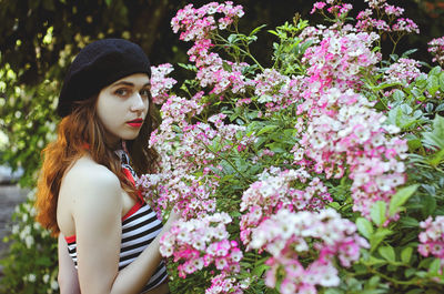 Portrait of young woman standing by flowering plants