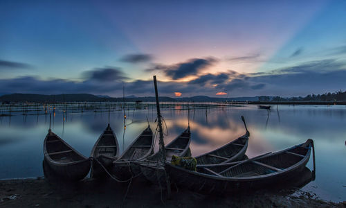 Boats moored in lake against sky during sunset