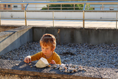 The blond boy is playing with stones. a  boy sits among the stones and plays enthusiastically.