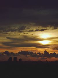 Silhouette cityscape against dramatic sky during sunset