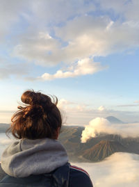Rear view of woman sitting on rock against sky