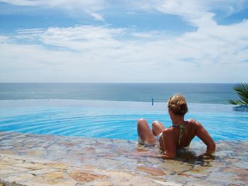 Rear view of shirtless man looking at swimming pool against sea