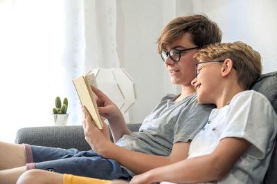 Brothers reading book on sofa at home