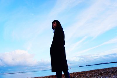 Woman standing by sea against blue sky