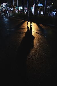 Silhouette man walking on illuminated street in city