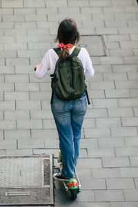 Rear view of woman standing on footpath against wall