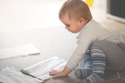 Baby boy with book sitting on mat at home