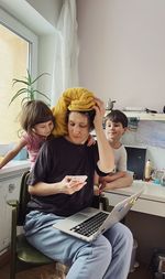 Woman sitting at her home office with two children curiously looking at her phone