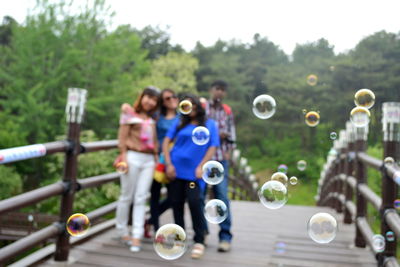 Bubbles in mid-air with happy friends standing on footbridge