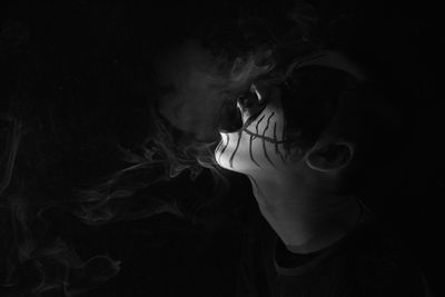 Close-up of man with face paint smoking against black background