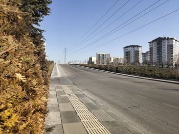 Empty road along plants and buildings against sky
