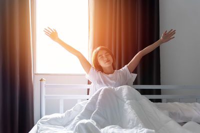 Rear view of woman with arms raised on bed at home
