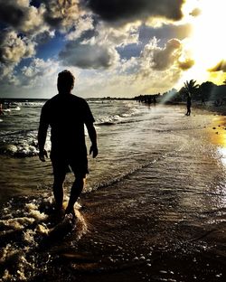 Rear view of man walking on beach during sunset