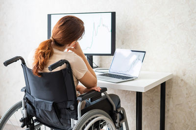 Rear view of woman looking at laptop while sitting on wheelchair