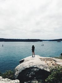 Rear view of woman standing on rock formation by river against sky