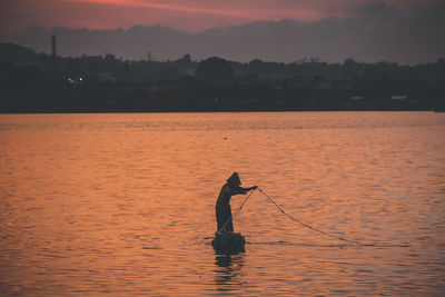 Silhouette man fishing in sea against orange sky