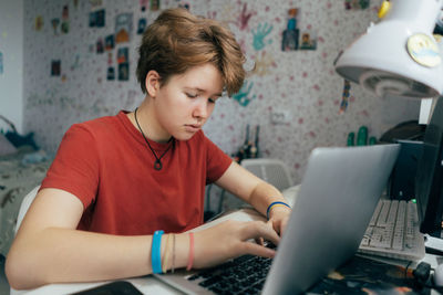 A teenage girl is studying online using a laptop while sitting at a table in the room.