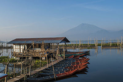 Boats moored by stilt house in lake against sky