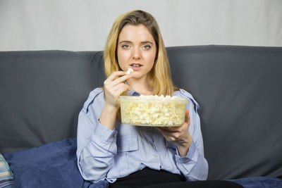 Portrait of young woman having popcorn while sitting on sofa at home