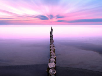 Wooden posts in sea against sky during sunset