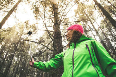 Low angle view of woman taking selfie with monopod by trees in forest