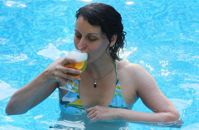 Woman drinking beer while swimming in pool