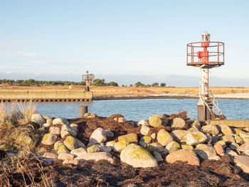 Red and white small technical lighthouse on the stony pier viewed from low angle with stony pier