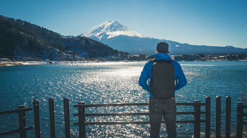 Rear view of man standing by lake against mt fuji in winter