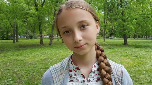 Portrait of teenage girl on field against trees at park