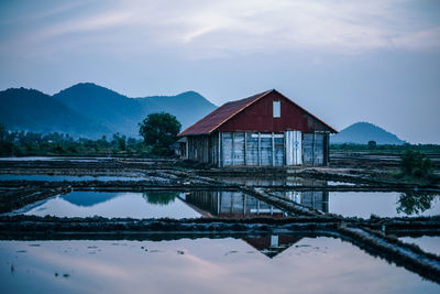 House by lake and buildings against sky