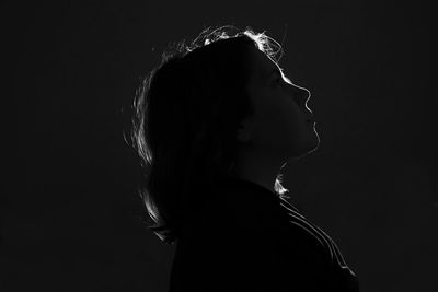 Side view of young woman standing against black background