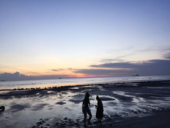 People standing on beach against sky during sunset