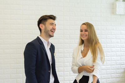 Cheerful business colleague talking while standing against white brick wall